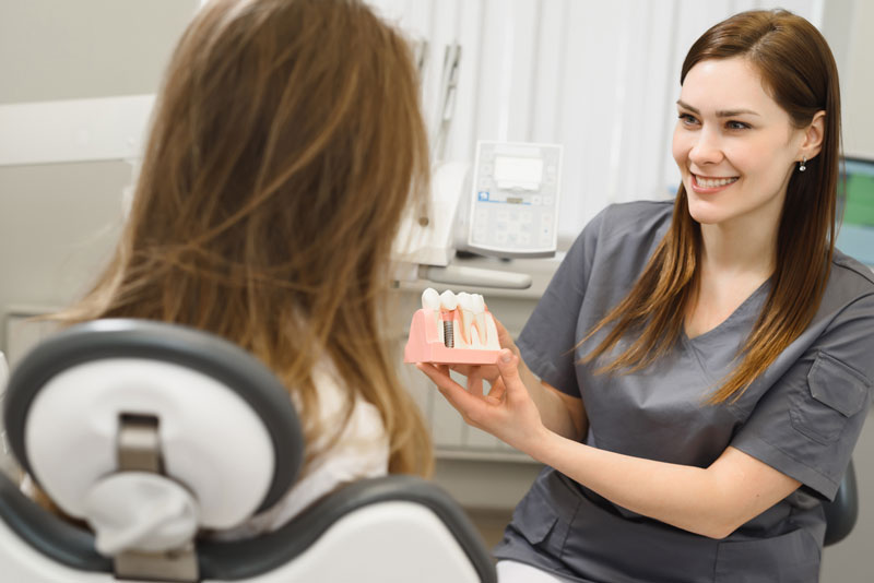 a doctor showing a dental implant model to a patient to show her how it can restore her smile after she becomes a candidate for dental implants.